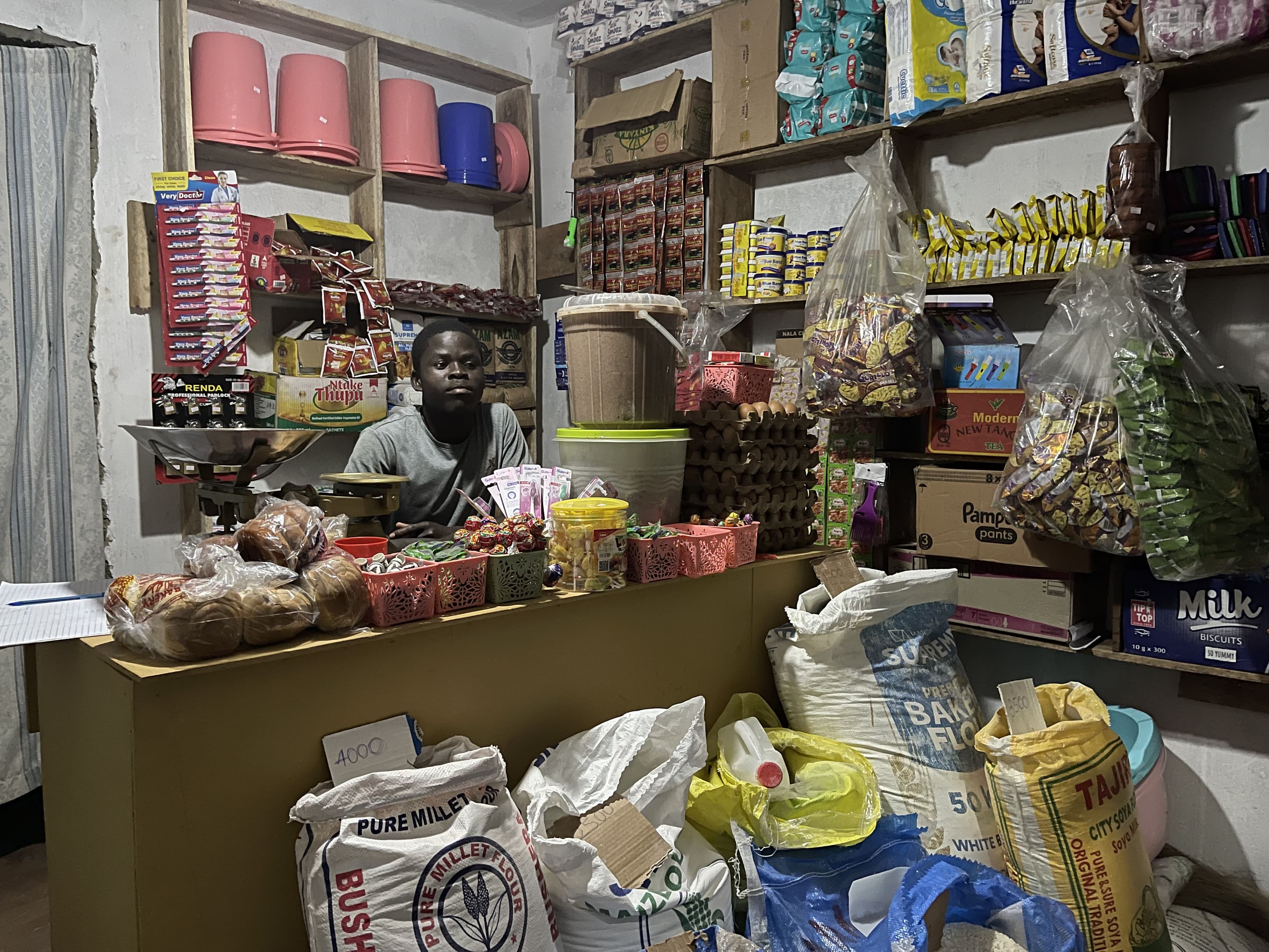 A shopkeeper behind the counter of a small, well-stocked village shop