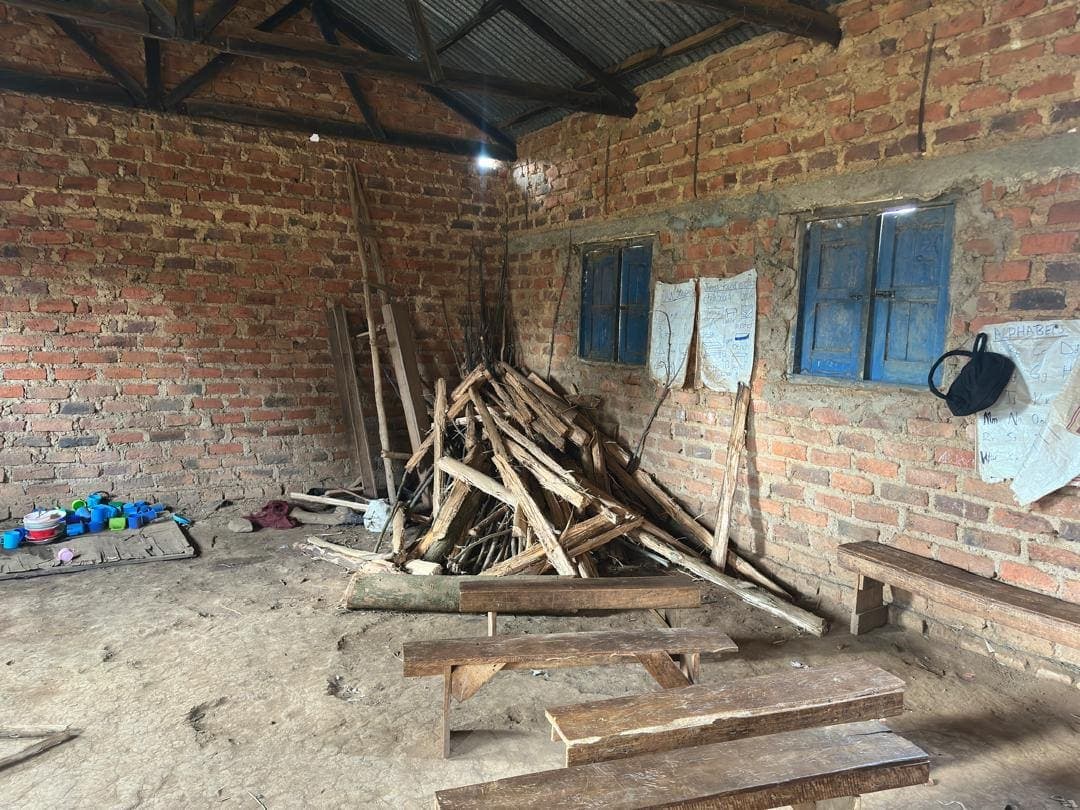A classroom with firewood stored on the dirt floor beside log benches
